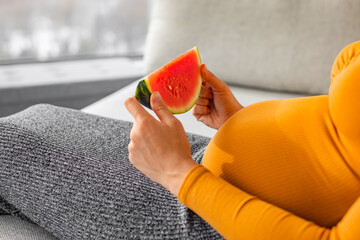 Pregnant woman eating watermelon slice during summer pregnancy. Sweet fruits craving, gestational...