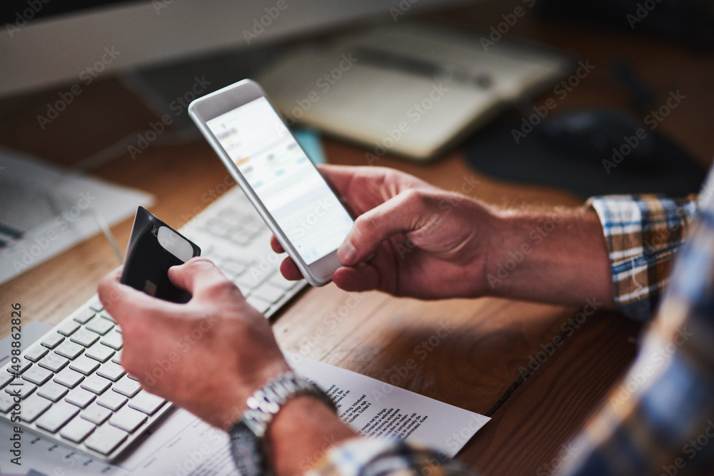 Poster You dont need to leave your desk to shop. Shot of an unidentifiable programmer holding his credit card while using his smartphone.