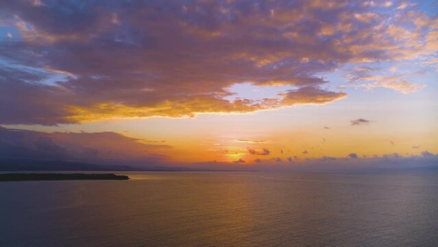 Sea sunset on the tropical coast. Orange sun glare behind lilac clouds in the blue evening sky. Nature sunset.