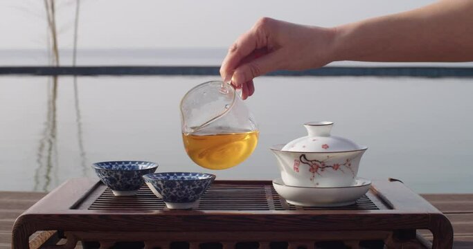 Beautiful Chinese tea ceremony near water slow motion eastern culture style. Female hand pouring fresh steaming drink into cups. Meditative calm mood and atmosphere