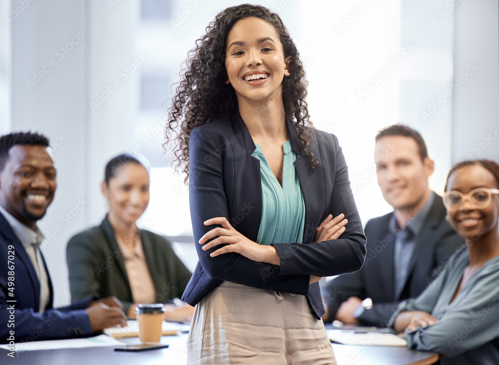 Poster Me and my team. Cropped portrait of an attractive young businesswoman standing in the boardroom with her arms folded and her colleagues in the background.