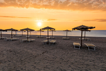  empty beach during beautiful sunrise or sunset with chaise loungues and nice umbrellas with blue sea