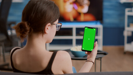 Closeup of young woman holding vertical smartphone with green screen in online conference or group...