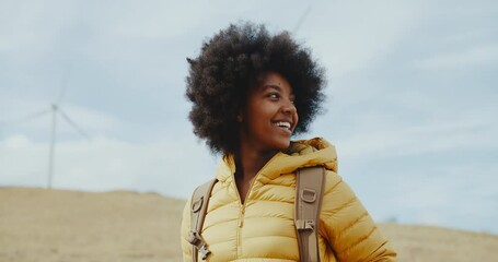 Portrait of young black woman on mountainside in front of windmills, clean energy, sustainability, and diversity
