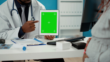 Male obstetrician using greenscreen template on tablet display, talking to pregnant woman. Specialist holding mockup background with blank copyspace and isolated chroma key. Close up.