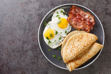 Savoury oat pancake perfect for breakfast with bacon and fried eggs close-up in a plate on the table. Horizontal top view from above