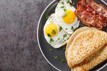 Staffordshire oatcakes with bacon and fried eggs close-up in a plate on the table. Horizontal top view from above