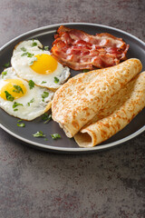English breakfast of bacon, eggs and oatcakes oat pancakes close-up in a plate on the table. Vertical