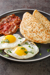 Traditional English Staffordshire oat pancakes, bacon and fried eggs close-up in a plate on the table. Vertical