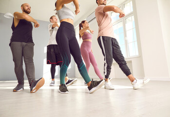 Group of energetic young people in activewear doing physical exercise at the gym. Team of happy fit men and women enjoying a fitness workout or dance class with a professional instructor. Cropped shot