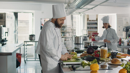 Authentic cook cutting coleslaw salad to make food recipe, using fresh ingredients in restaurant kitchen. Male chef using knife on cutting board to slice celery for gourmet dish.