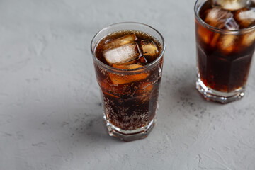 Cold Refreshing Dark Cola with Ice Cubes on a gray background, side view.
