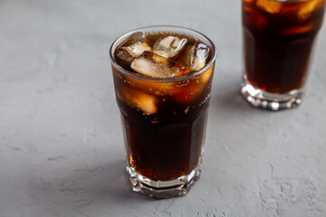 Cold Refreshing Dark Cola with Ice Cubes on a gray background, side view.