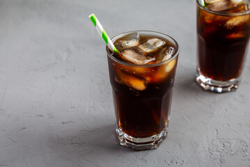 Cold Refreshing Dark Cola with Ice Cubes, Straws on a gray background, side view.