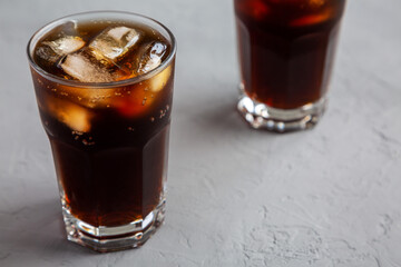 Cold Refreshing Dark Cola with Ice Cubes, Straws on a gray surface, side view.