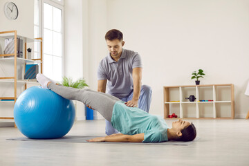 Male physiotherapist at rehabilitation center helping his female patient do physical exercises with...
