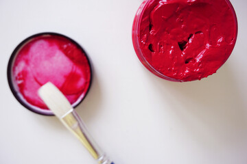 Close up top view of a opened red acrylic paint with the cap and paint brush on the side