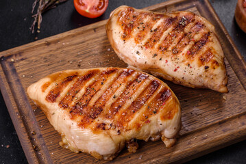 Delicious fresh grilled chicken fillet with spices and herbs on a dark concrete background