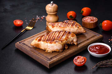 Delicious fresh grilled chicken fillet with spices and herbs on a dark concrete background