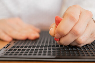 A woman uses a special stencil and stylus to write a letter in braille. 