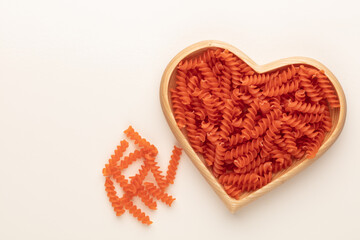Red lentil fusilli pasta in a heart shaped wood bowl.