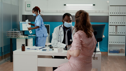 Pregnant patient meeting with doctor in cabinet during covid 19 pandemic to receive childbirth advice. Woman expecting child attending checkup consultation with health specialist.