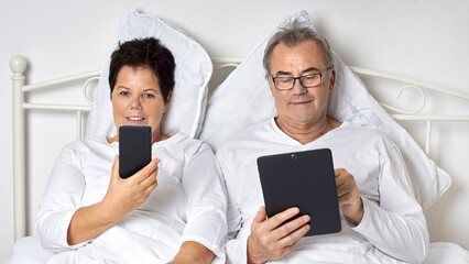 elderly couple stay in bed with computer