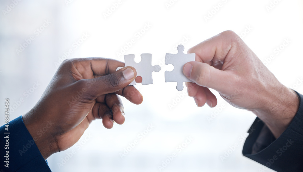 Poster Problems are better solved together. Cropped shot of two unrecognizable businesspeople completing a puzzle together in a modern office.