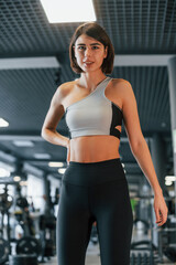 Standing and taking a break. Woman in sportive clothes with slim body type is in the gym