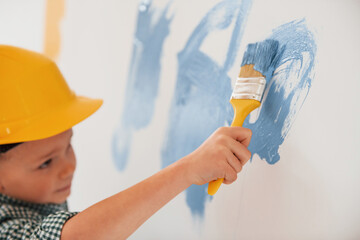 Using blue and yellow colors. Little boy painting walls in the domestic room