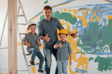 Three people. Man with two little boys standing in the domestic room. Conception of repair and renewal