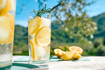 Summer refreshing lemonade drink or alcoholic cocktail with ice, rosemary and lemon slices on the...