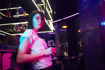 Woman with brown hair standing in the night club and holding drink