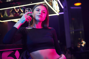 Fototapeta na wymiar Young woman standing in the night club with drink in hand