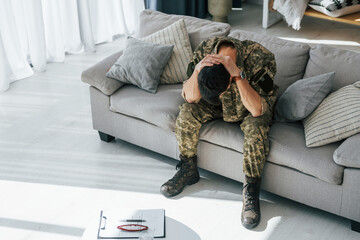 Bad mood. Post traumatic stress disorder. Soldier in uniform sitting indoors