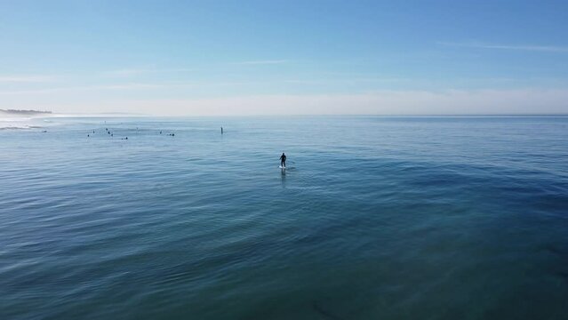 A beautiful aerial drone shot, drone tracking a man paddling with his sup board in the ocean close to the beach, Carlsbad State Beach - California