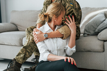 Soldier with his wife sitting indoors and embracing