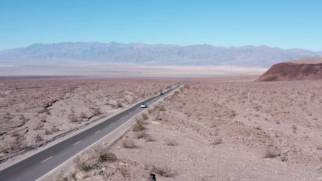 White Car Driving On Asphalt Road Through The Desert Sands. Scenic Imagery, Mountains In The Background