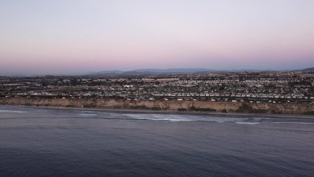 A beautiful aerial drone shot, flying towards the coast with a view of a town, the horizon, and mountains, Carlsbad State Beach - California