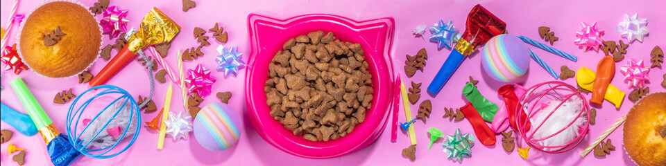 Pet cat happy birthday background with set different cats and kitty snack, food and toys, cat muzzle shape bowl, birthday cupcakes with happy birthday candles, accessories. Flatlay on pink background