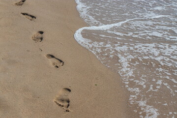 Footprints in the sand beach. Footprints in the sand against a sea wave. Footprints on a sunny day with golden sand, beach, wave and footsteps