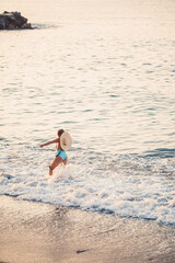 Beautiful girl in a blue swimsuit and hat on a sandy beach at the sea in the sunset sunlight