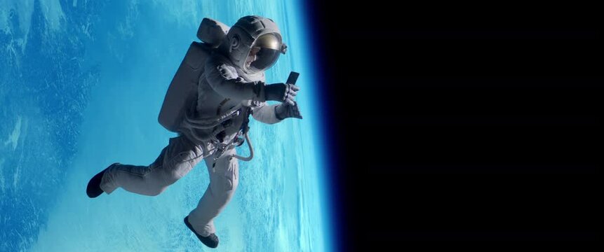 Female astronaut having a video call on her phone while performing space walk in open space, Earth in the background. Shot with 2x anamorphic lens