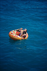 Beautiful young woman fell from an inflatable circle into the blue sea. Girl on vacation swims with a circle on the sea