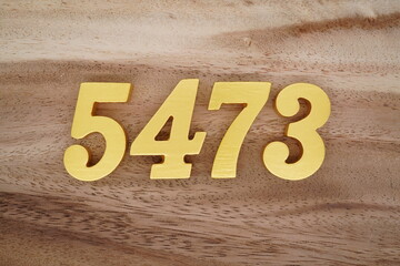 Golden Arabic numerals on a real brown and white wooden floor number 5473