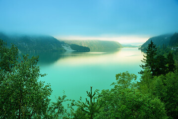 interesting morning mood, turquoise lake Achensee, clouds above and light spot from clearing fog © SusaZoom