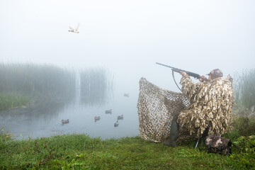 Camouflaged hunter shooting into sky during duck hunting.