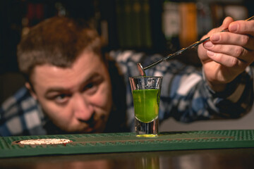 Bartender taking out bar spoon from shot glass with green drink