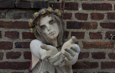 A young girl is dressed as a Halloween horror figure. 
She wears filthy rags as clothing and has a thorny 
crown with flowers on her head. She is seen begging 
with her hand reaching out.
