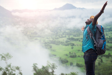 Freedom african traveler man carrying a backpack stands at the top of a mountain on a foggy...